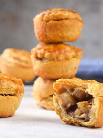 Mini apple pies stacked and one sliced open.