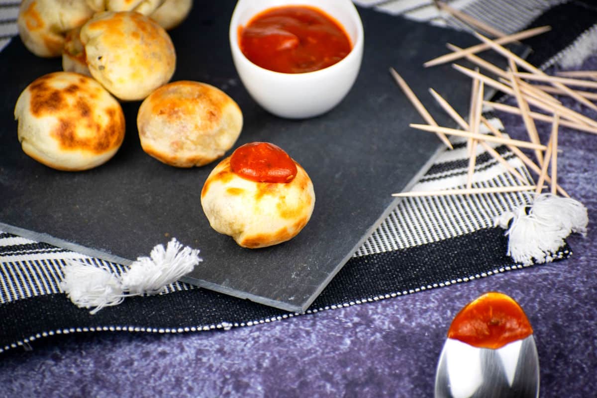 Mini pizza bites with marinara sauce and toothpicks on the side.