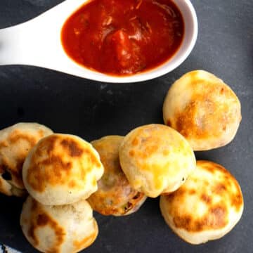 Mini pizza bites on black board with marinara sauce.