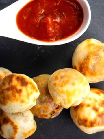 Mini pizza bites on black board with marinara sauce.