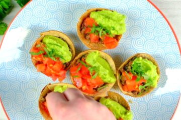 Taco cups with guacamole on decorative plate.