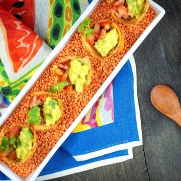 Baked taco cups in white dish with lentils on decorative cloth.
