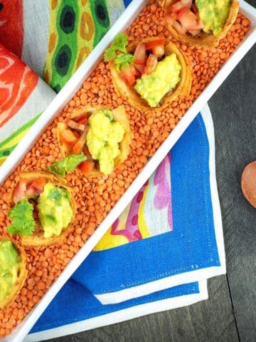 Baked taco cups in white dish with lentils on decorative cloth.