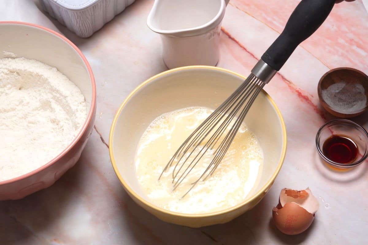 Pancake batter liquid ingredients in bowl with whisk.