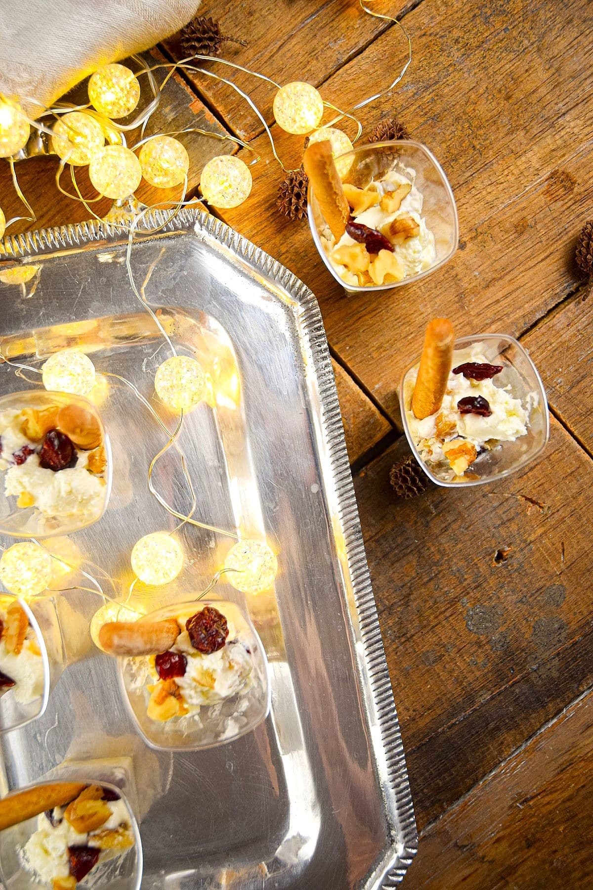 Goat cheese shots with mini breadsticks on wooden background and Christmas lights on the side.