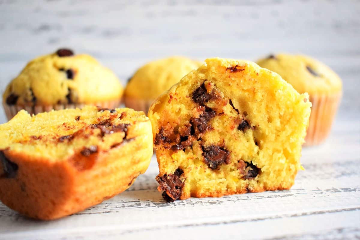 Orange chocolate chip muffin cut open on white wooden background.