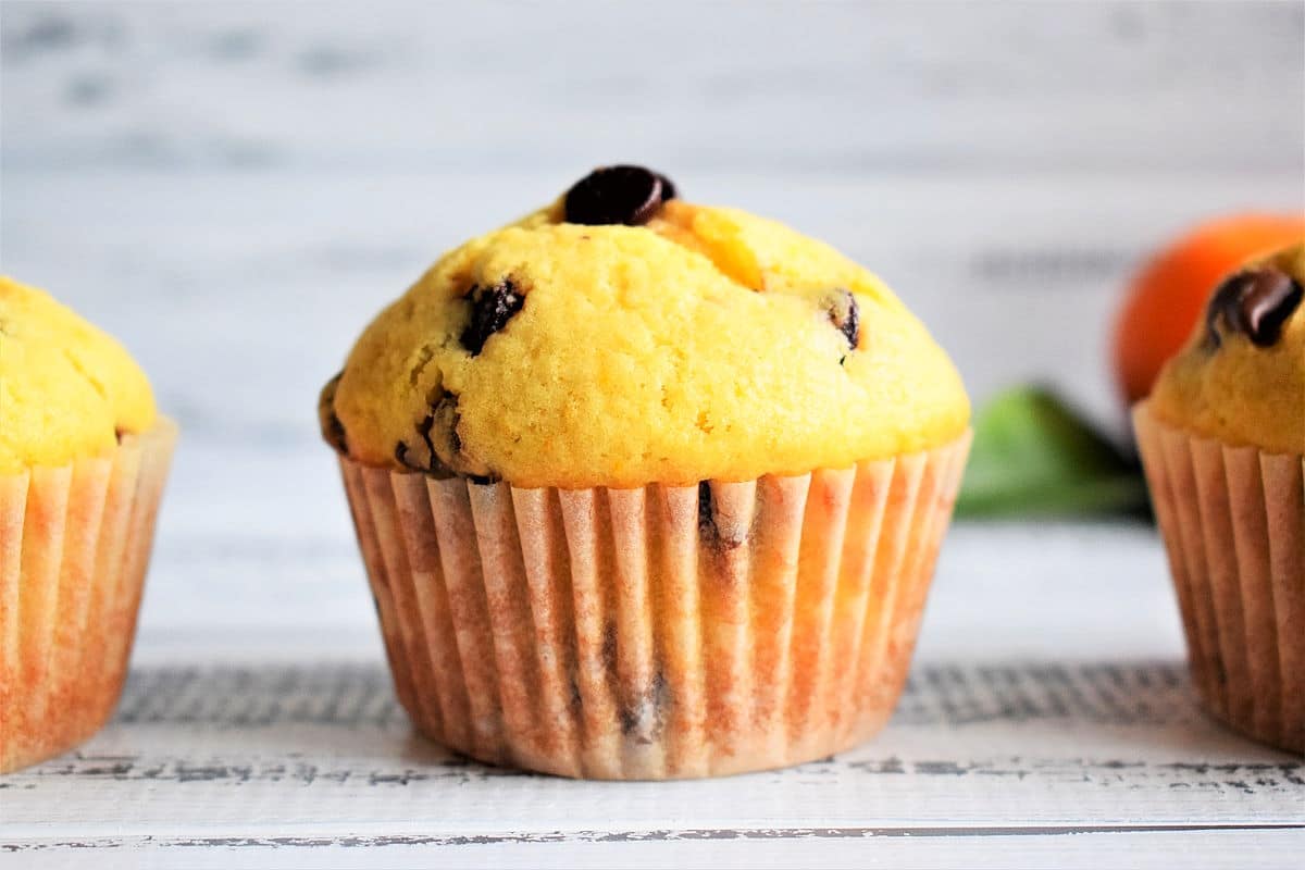 Orange chocolate chip muffins on white wooden background.