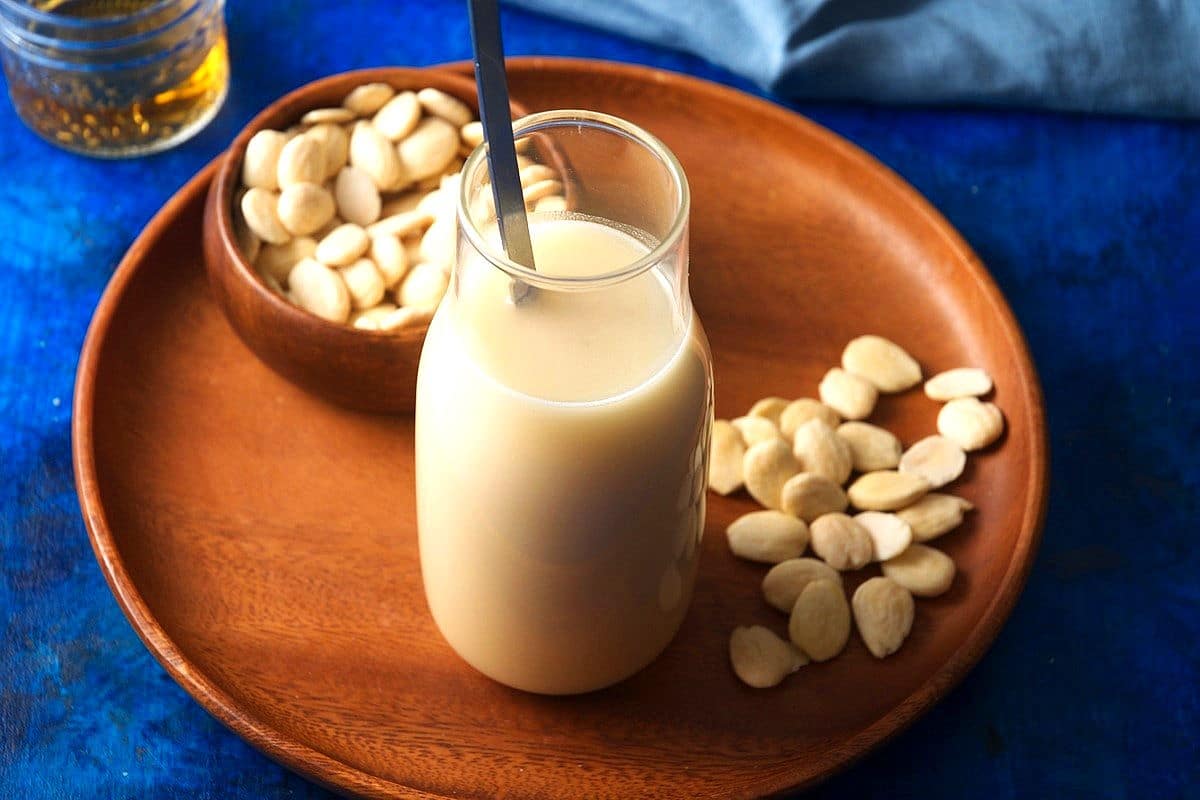 Orgeat almond syrup in jar with blanched almonds on the side.