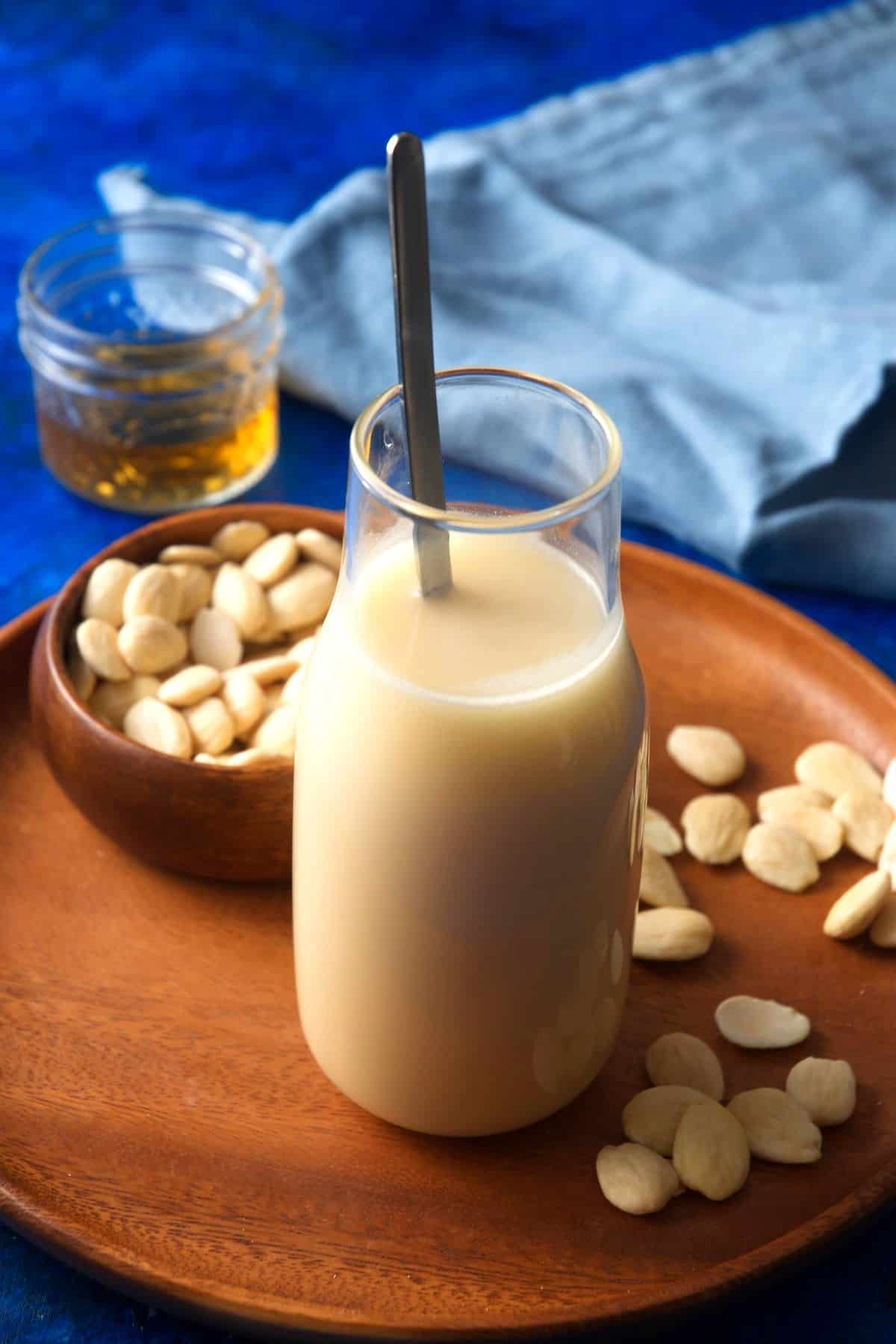 Orgeat syrup in jar with spoon and blanched almonds on the side.