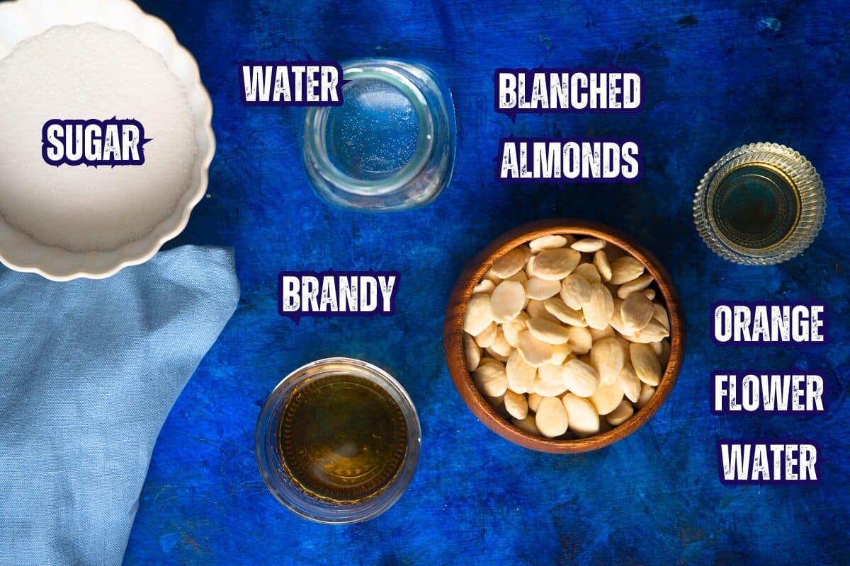 Blanched almonds, sugar, brandy and orange flower water prepped and labeled on blue background.