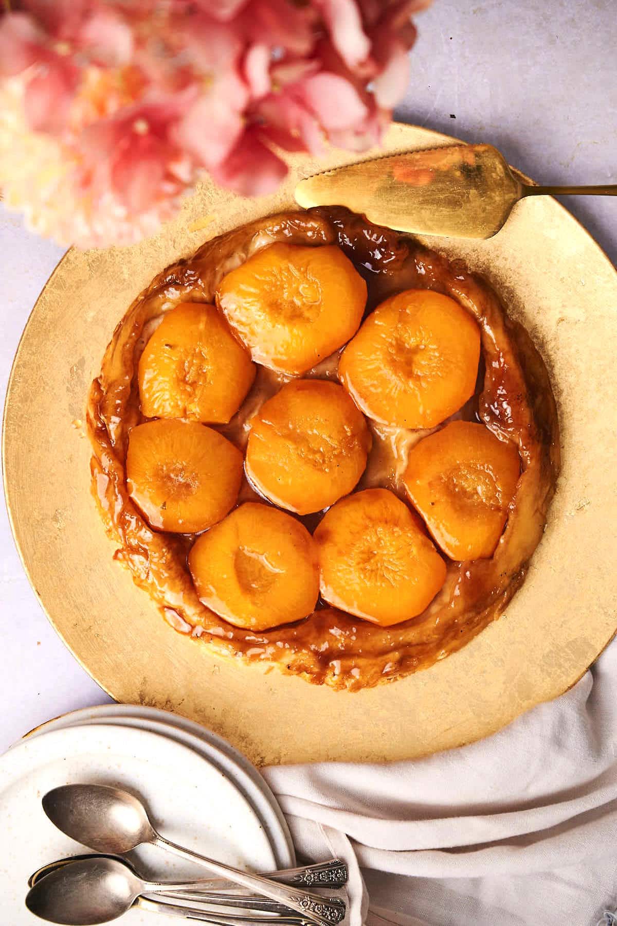 Peach tarte tatin on serving tray with golden pie server and spoons on the side.