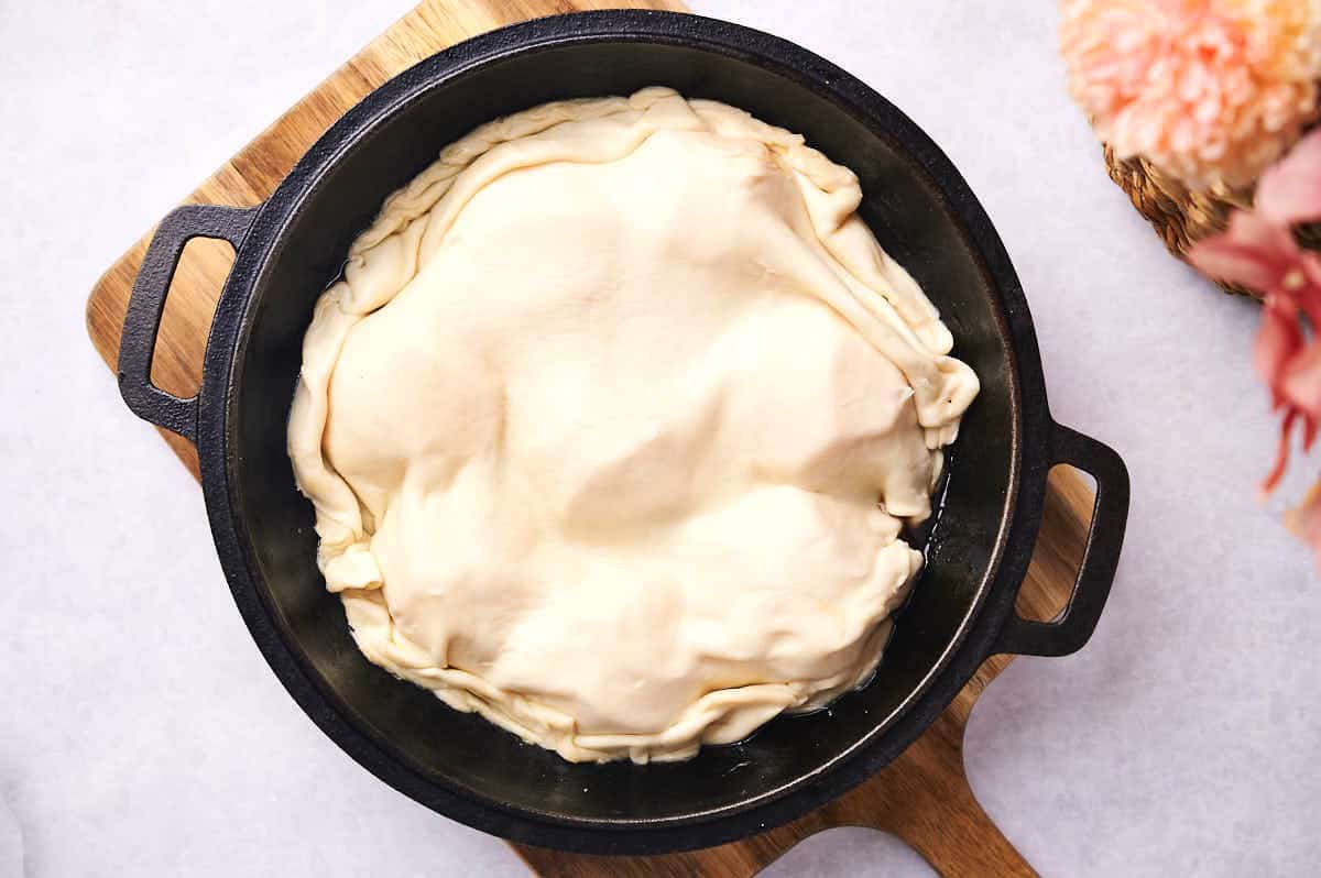 Puff pastry over peaches in pan.