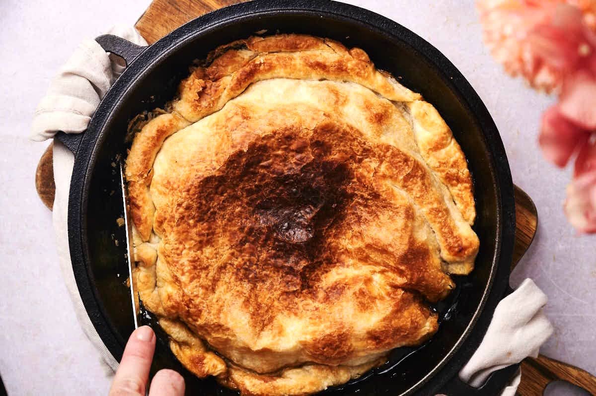 Knife loosening a peach tarte tatin in cast iron pan.