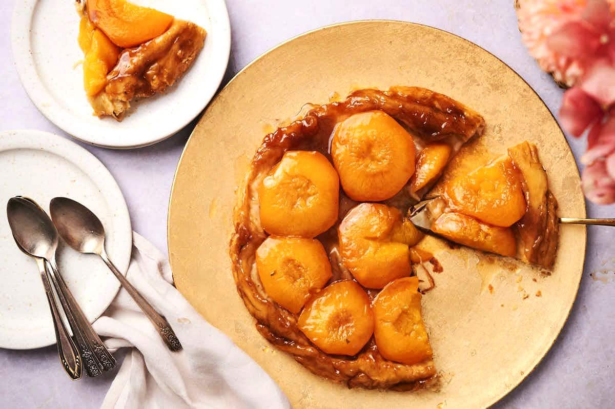 Peach tarte tatin on golden serving tray with a slice missing.