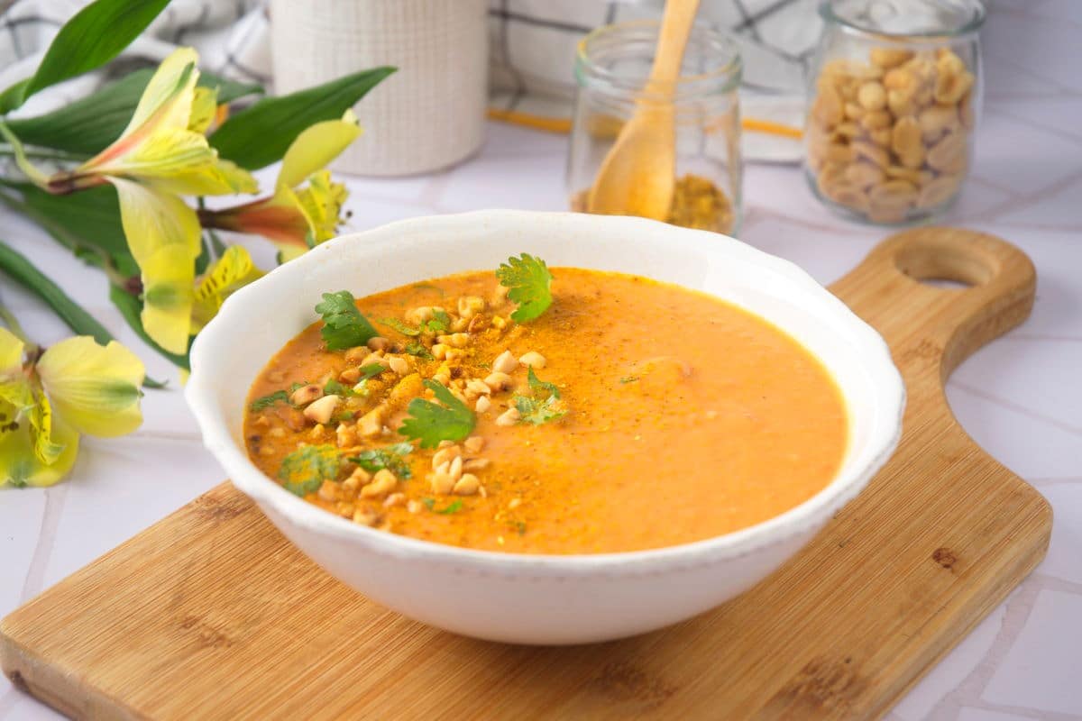 Peanut butter soup in a white bowl with chopped peanuts and cilantro.