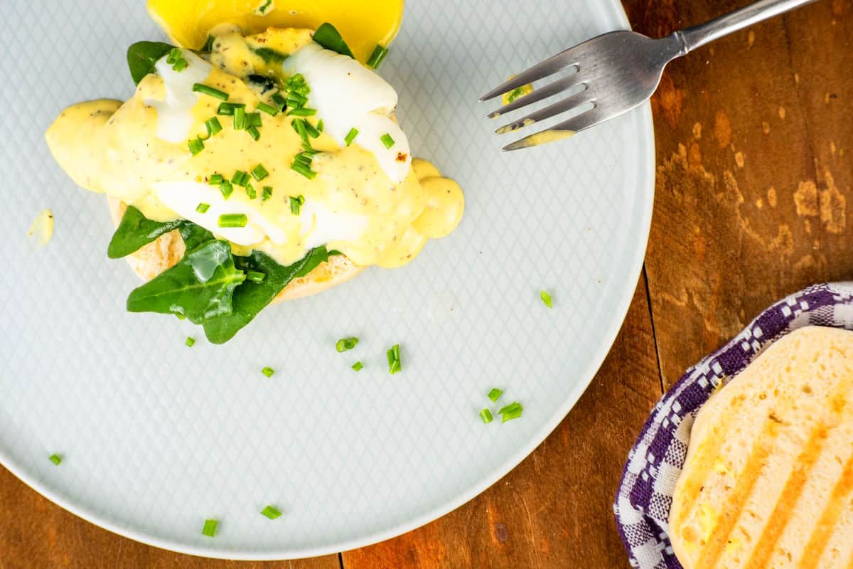 Poached egg with mock bearnaise sauce and spinach on a white plate with fork on the side.