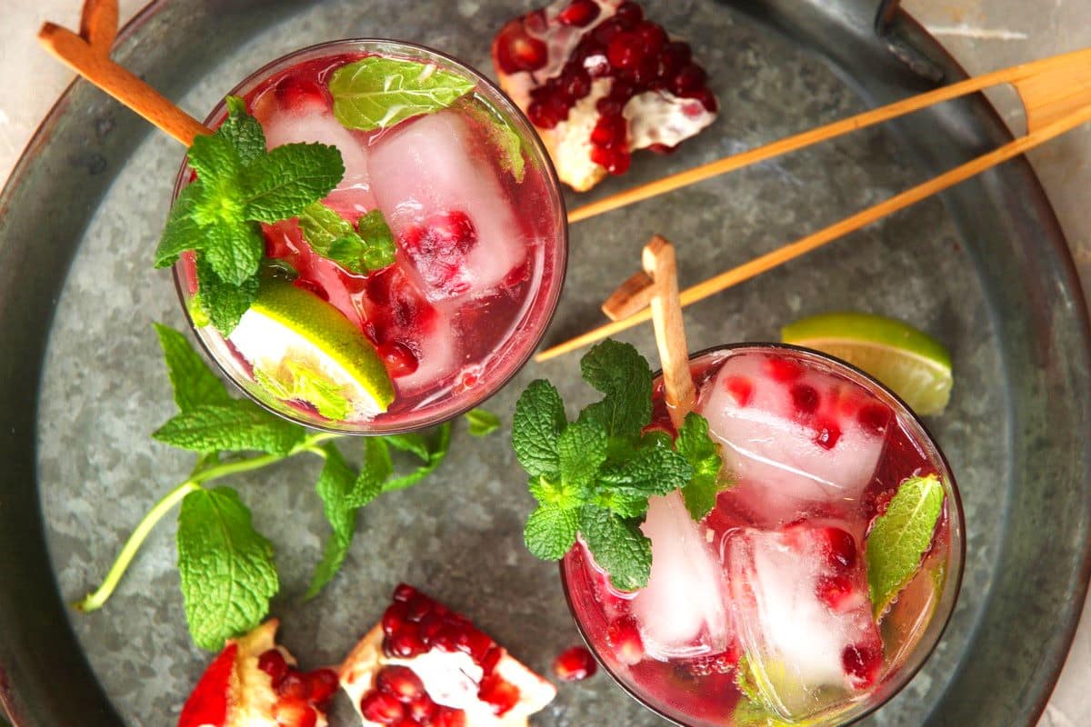 Pomegranate mojito mocktail in glasses with wooden swizzle sticks.