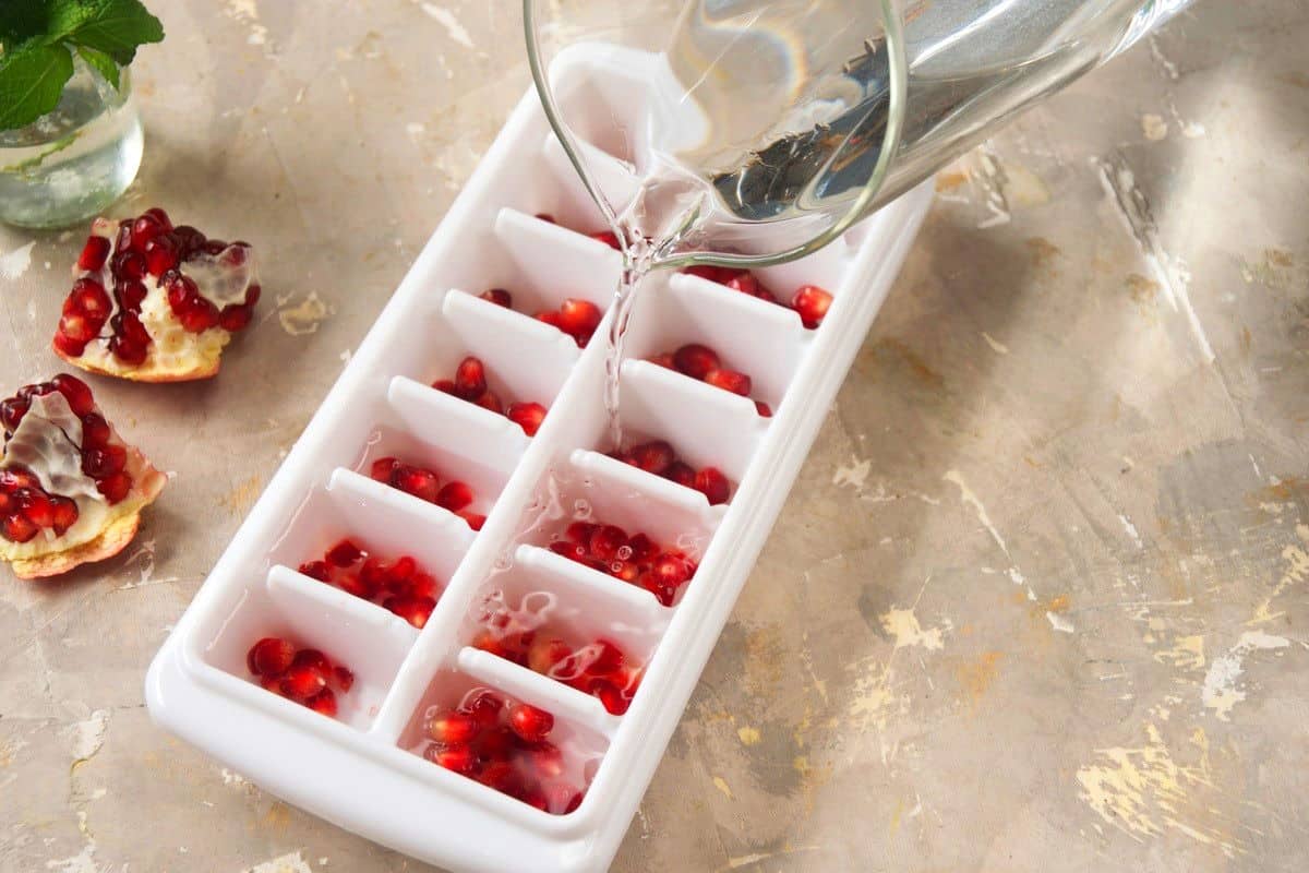 Pomegranate arils in ice cube tray with water.
