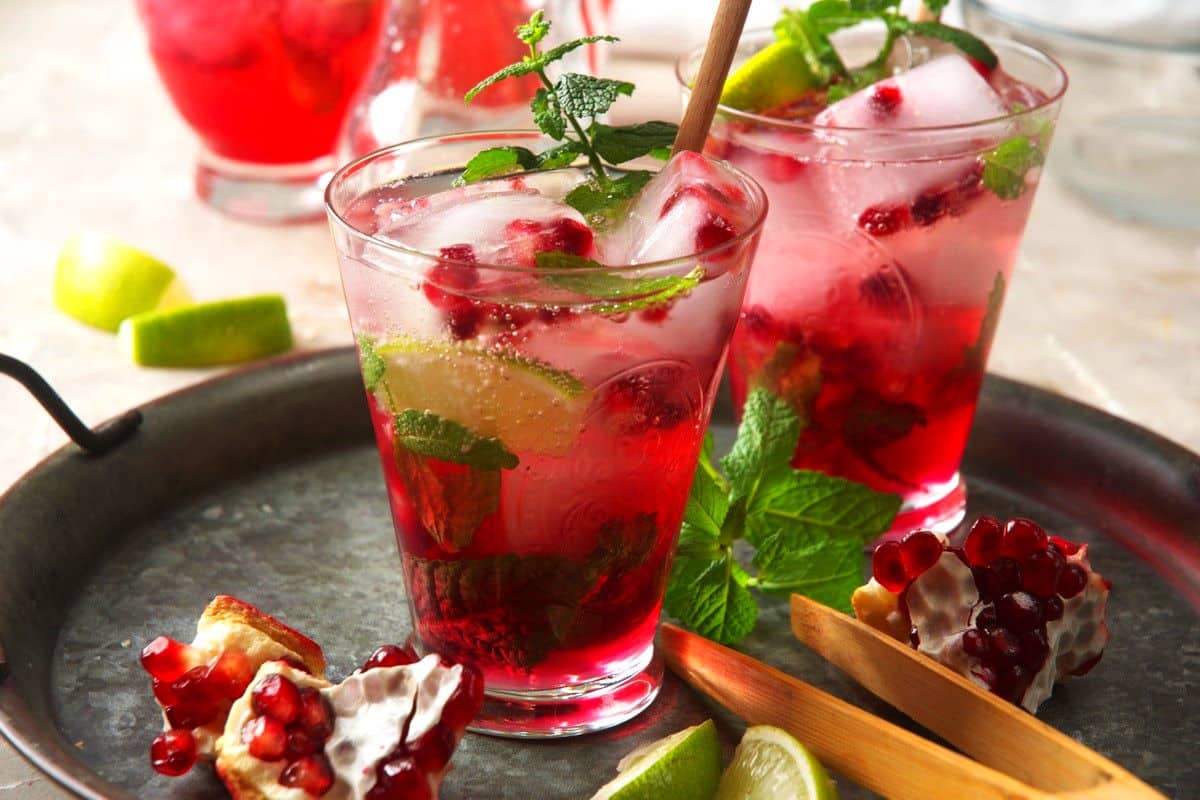 Pomegranate mojito mocktail in glasses with stirring stick.