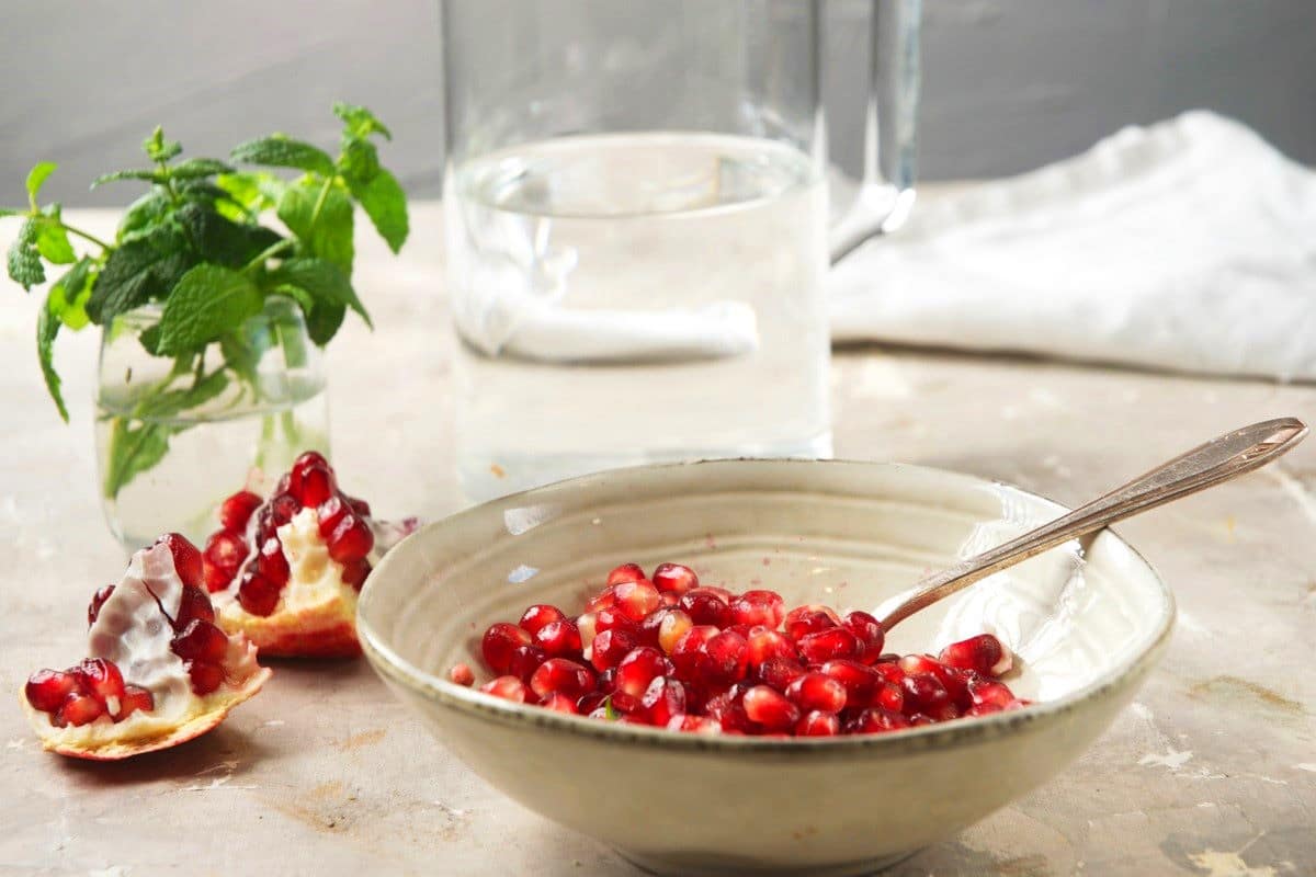 Pomegranate seeds in bowl with spoon.