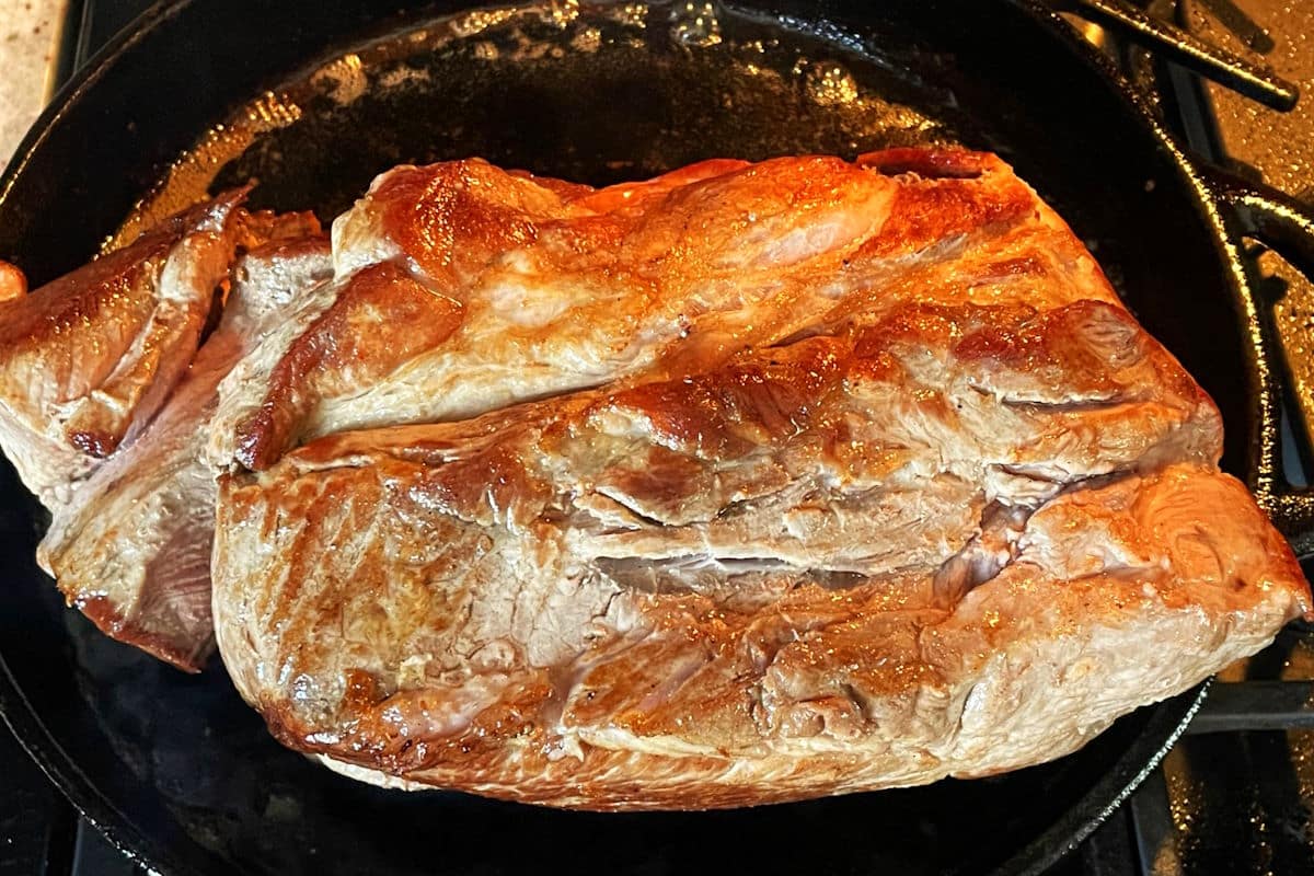 Seared pork shoulder roast in cast iron pan.