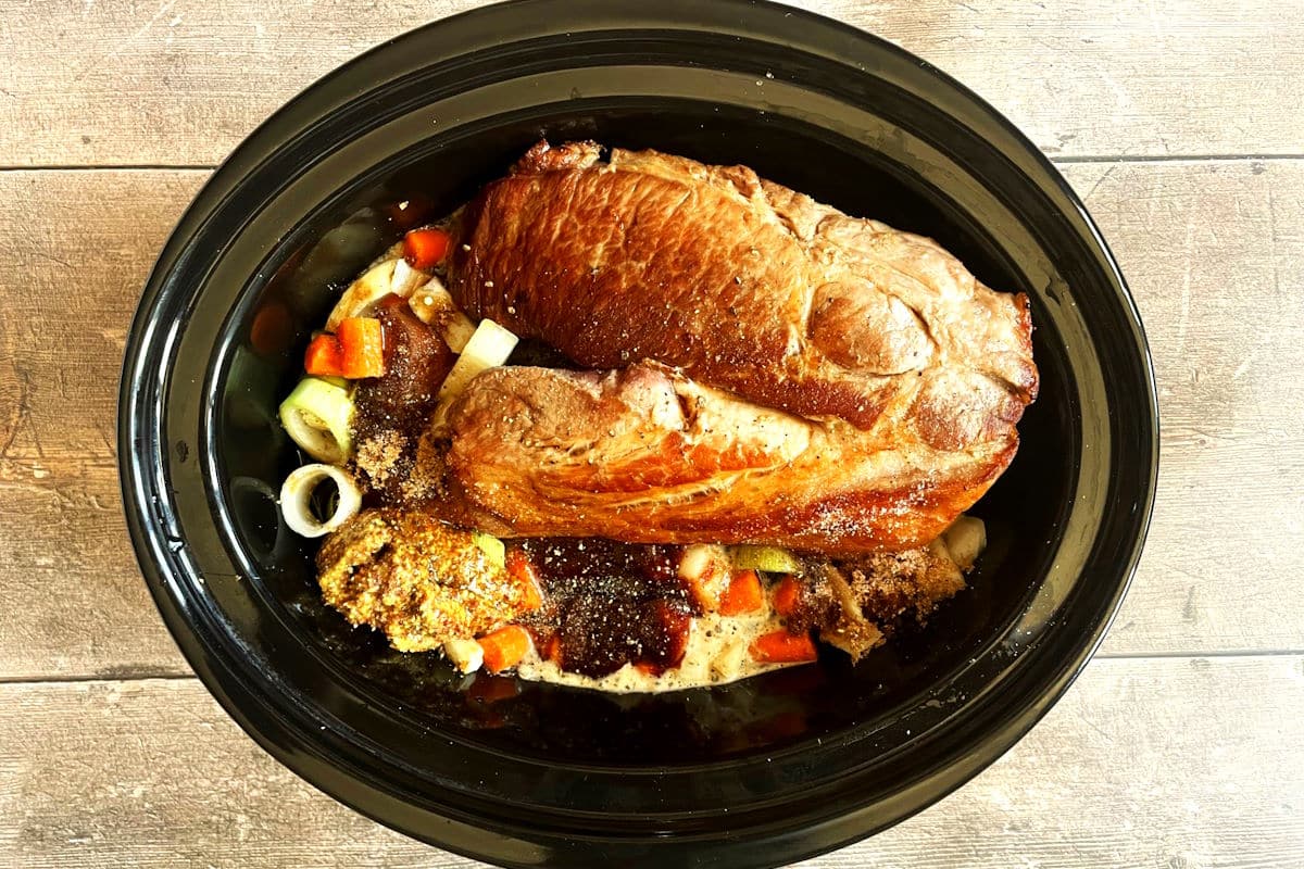 Seared pork shoulder roast, vegetables and beer sauce in slow cooker.