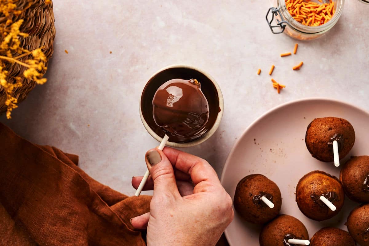 Pumpkin cake pop getting dipped and coated in melted chocolate.