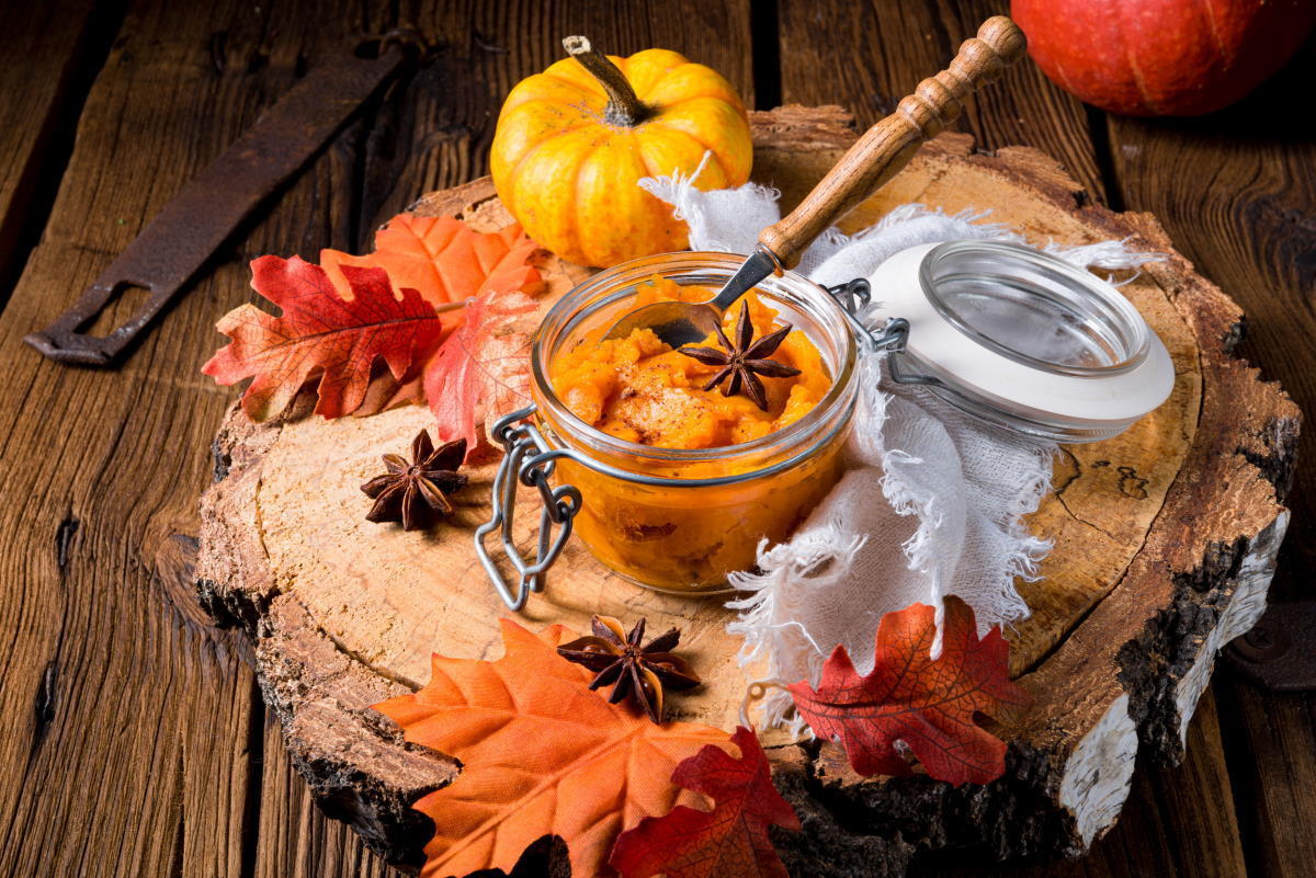 Pumpkin pie filling in a small jar on wooden background, fall leaves and gourds on the side.