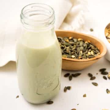 Pumpkin seed milk in glass with pumpkin seeds on the side.
