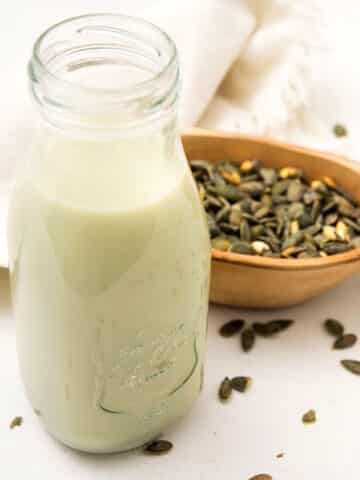 Pumpkin seed milk in glass with pumpkin seeds on the side.