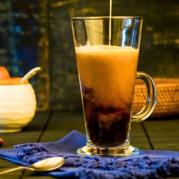 Pumpkin spice coffee creamer pouring into glass mug of coffee.