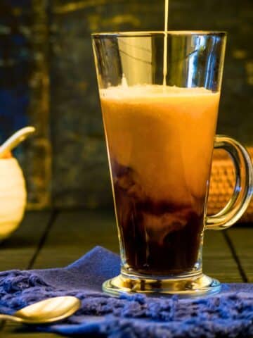 Pumpkin spice coffee creamer pouring into glass mug of coffee.