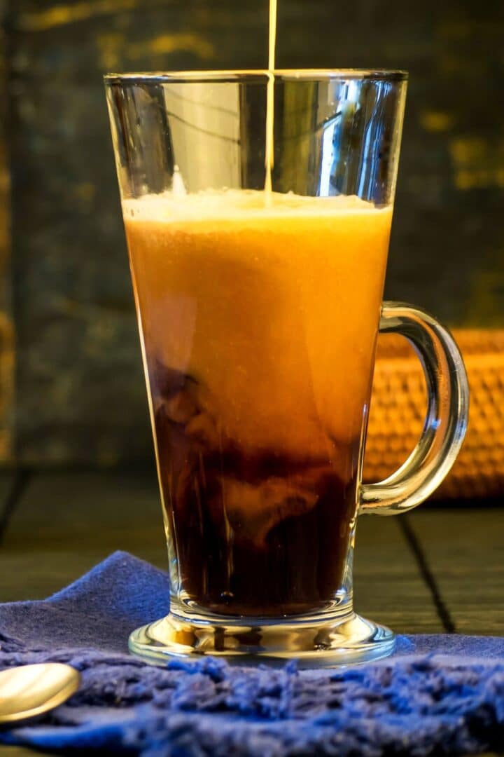 Pumpkin spice coffee creamer pouring into clear coffee mug.