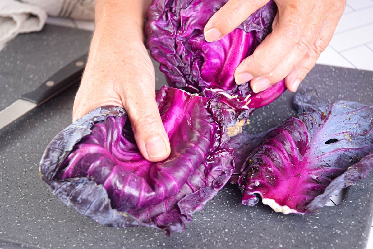 Purple cabbage held by hands on cutting board.