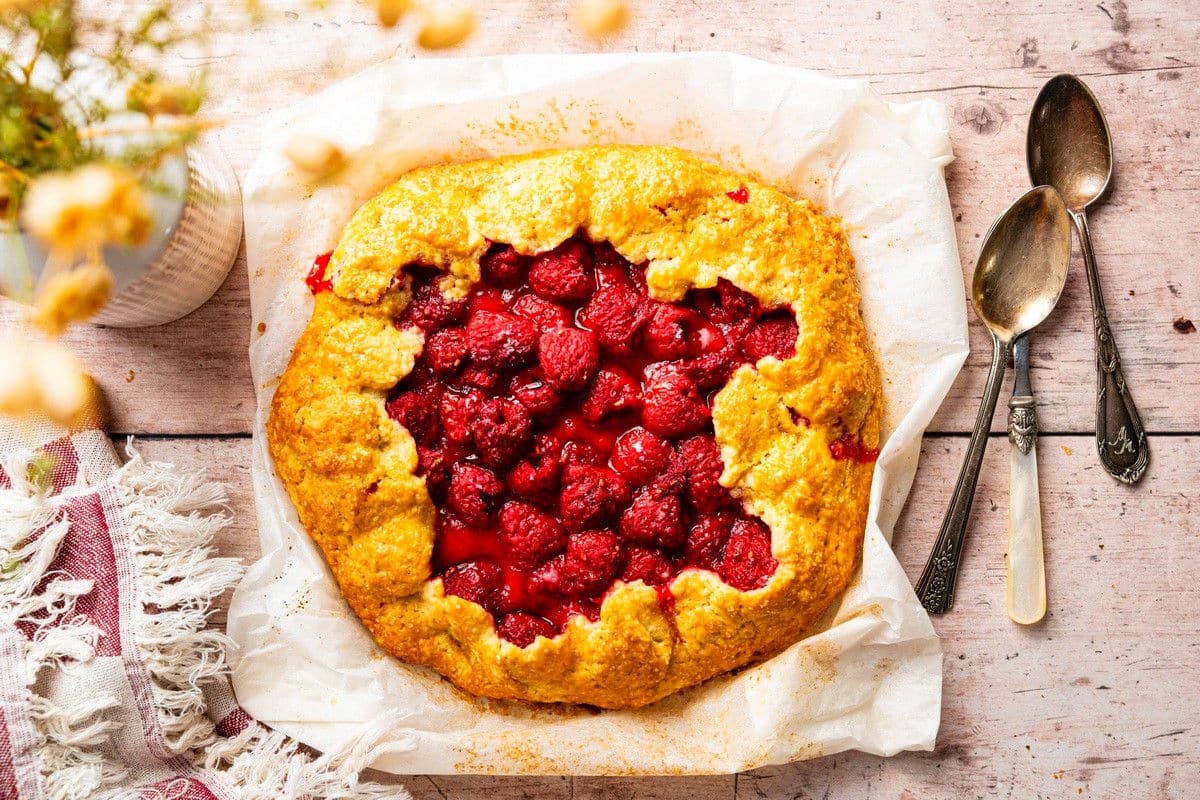 Raspberry galette on parchment with serving spoons on the side.