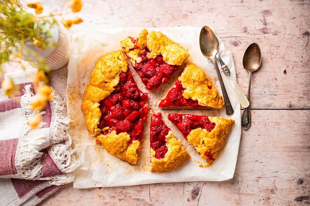 Sliced raspberry galette on parchment with spoons on the side.