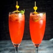 Raspberry twist cocktail in champagne glasses with lemon twist.
