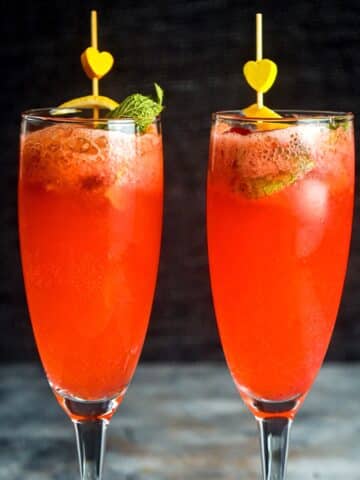 Raspberry twist cocktail in champagne glasses with lemon twist.