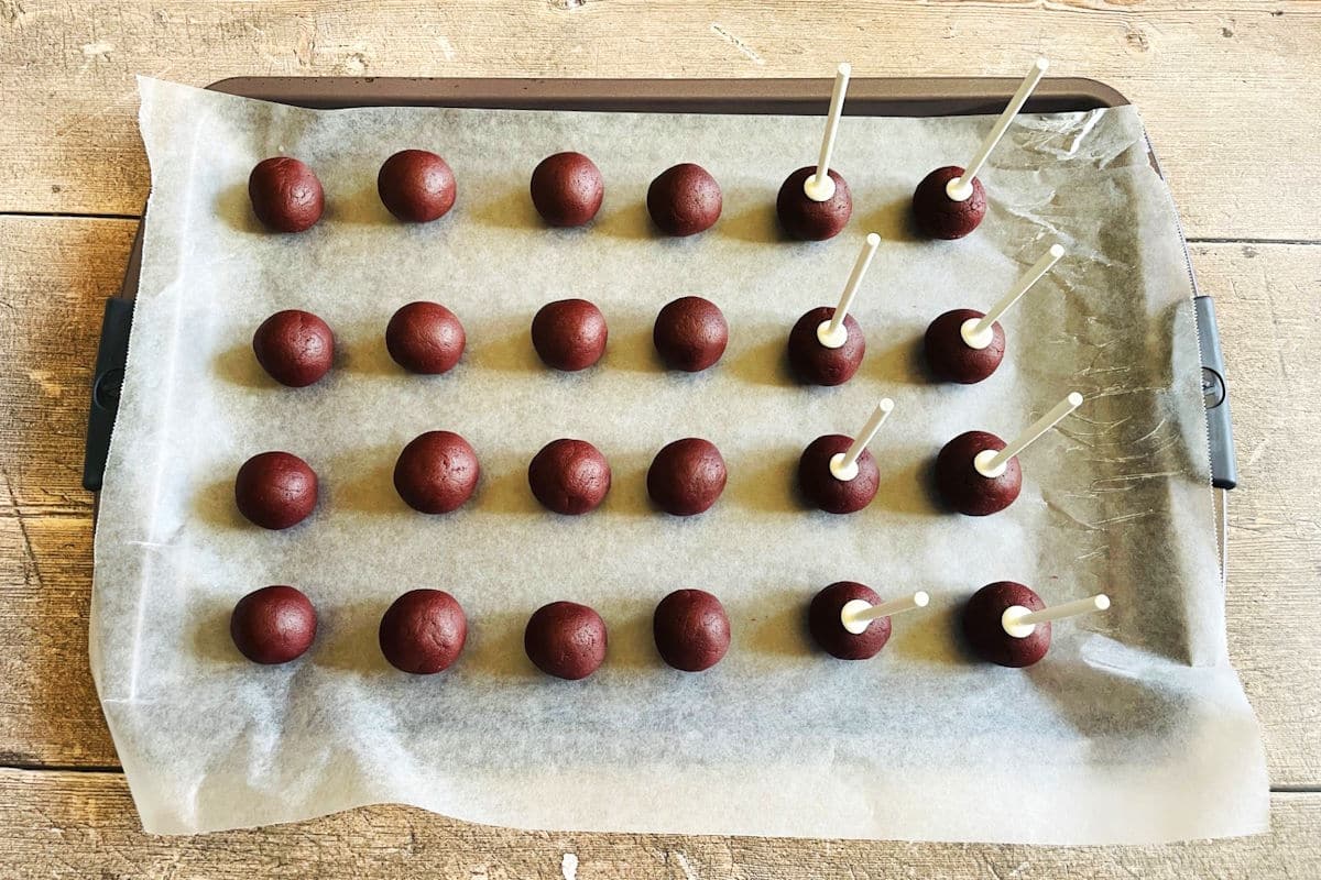 Red velvet cake balls on sheet pan with treat sticks.