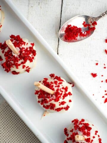 Red velvet cake pops in white dish on white wooden background.