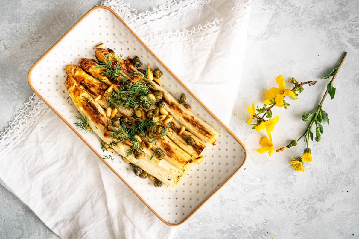Roasted white asparagus in serving dish with small yellow flowers on the side.
