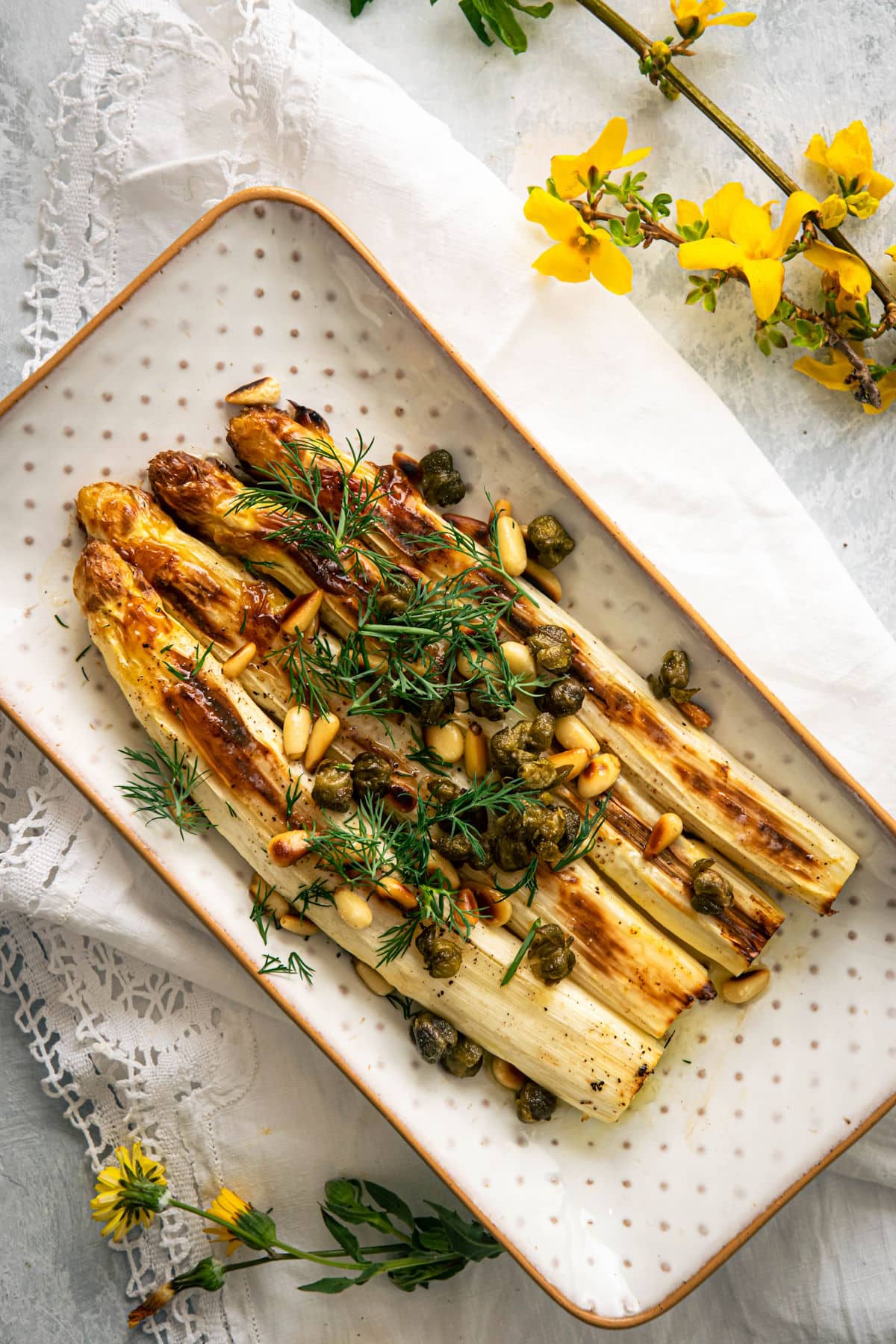 Roasted white asparagus on white dish with capers and dill.