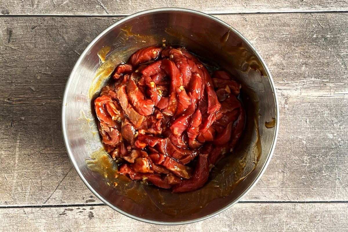 Raw beef strips in a bowl with teriyaki sauce.