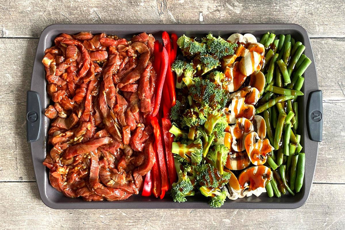 Raw beef strips and veggies on sheet pan with teriyaki sauce.