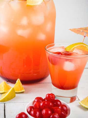 Shirley temple in glass and dispenser with maraschino cherries and orange wedges.