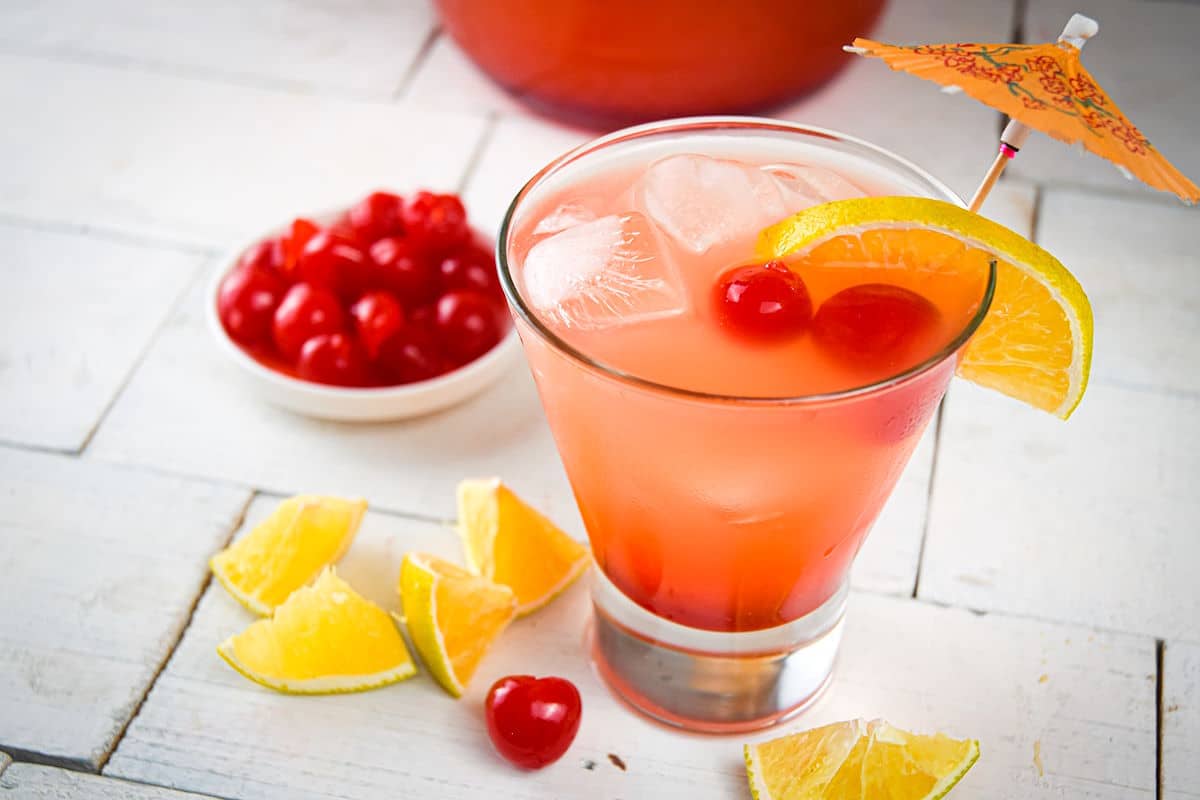 Shirley temple in glass with maraschino cherries, orange wedges and umbrella.