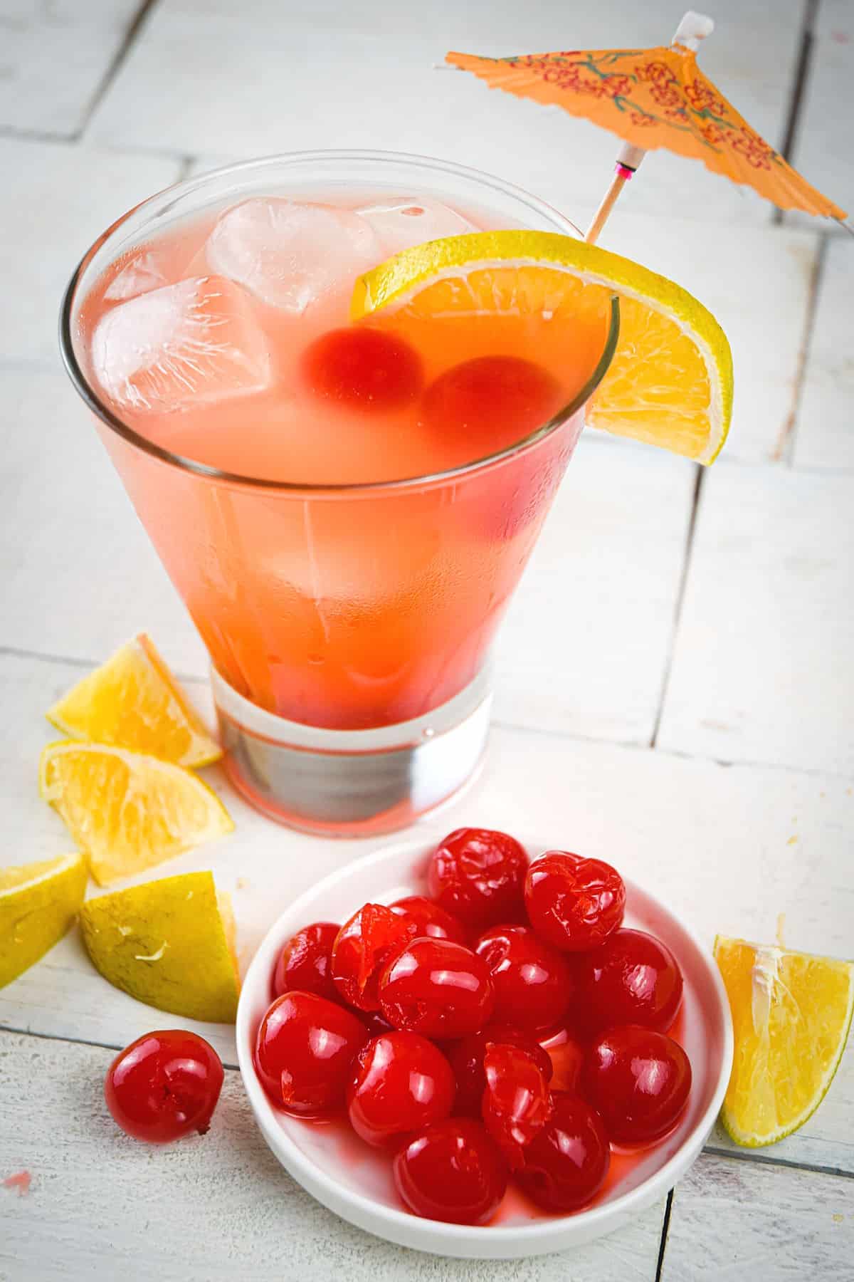 Shirley temple in glass with orange wedges and maraschino cherries on brick background.
