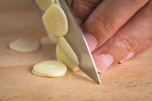 Thin slices of garlic on cutting board with a knife.