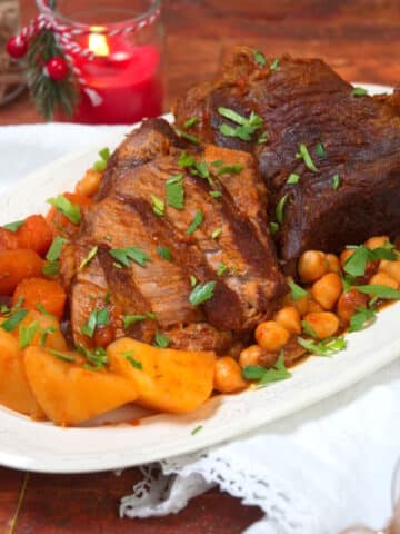 Sliced bison roast on white serving dish with vegetables.