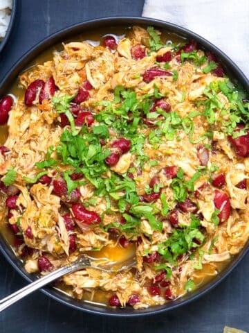 Mexican shredded chicken with salsa verde in dark bowl with spoon over rice.